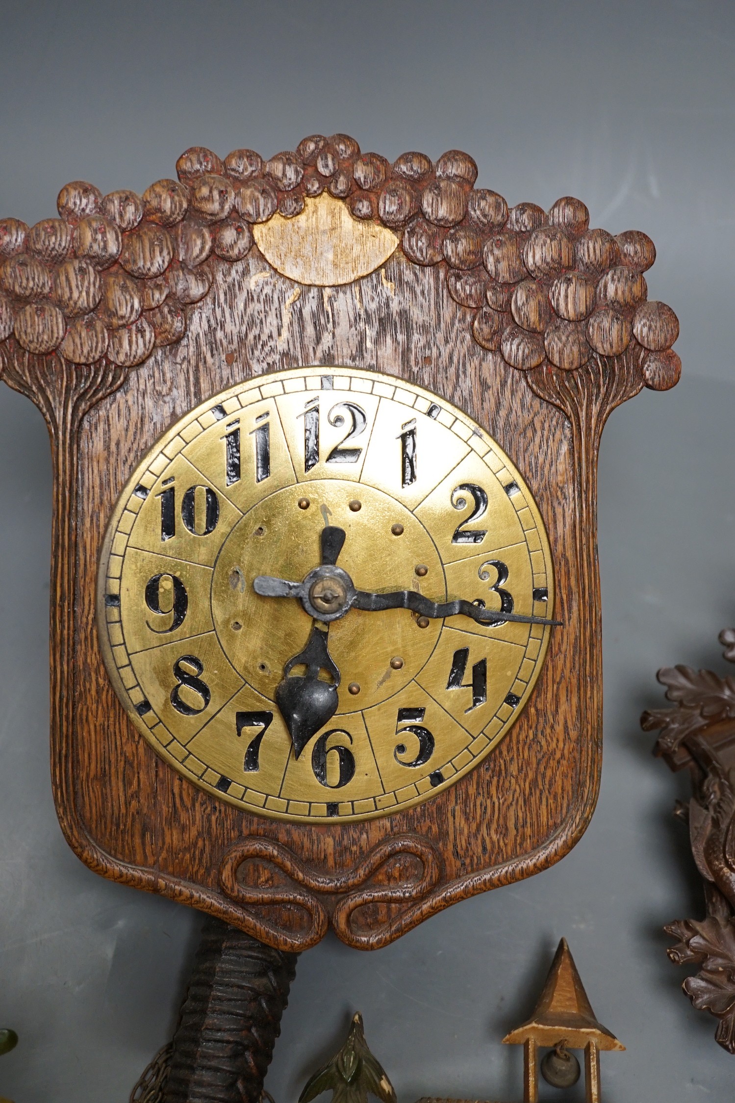 An early 20th century German Jugendstil oak wall timepiece, four miniature Black Forest timepieces and three floral enamelled examples, largest 23cms high